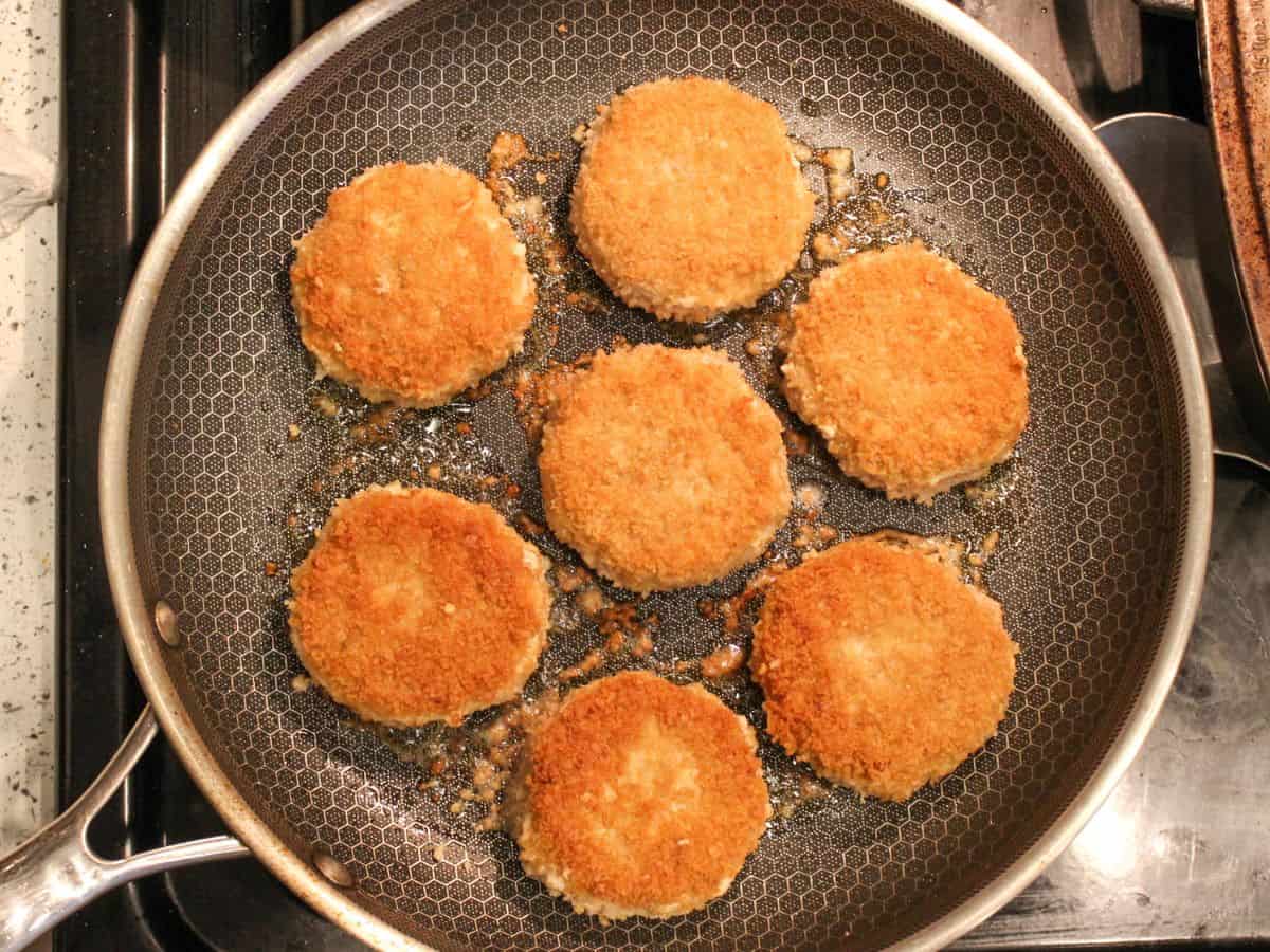 Seven browned chicken rissoles on a frying pan.