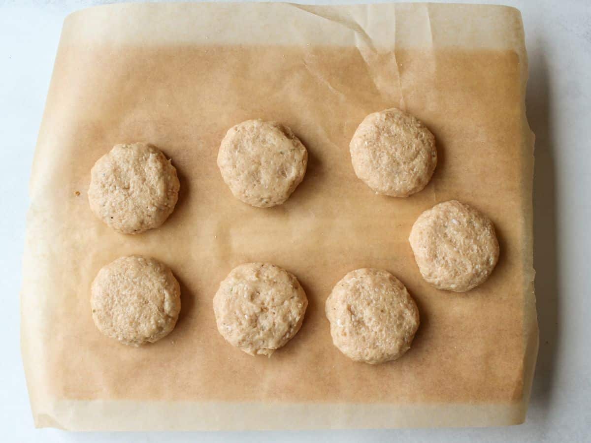 Seven uncooked meat patties on a parchment paper.