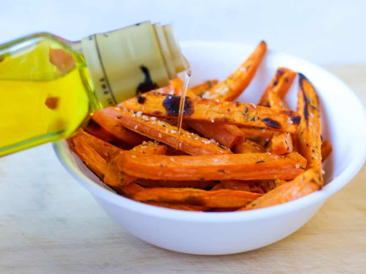 Oil drizzled over the white bowl with cooked sweet potato fries.