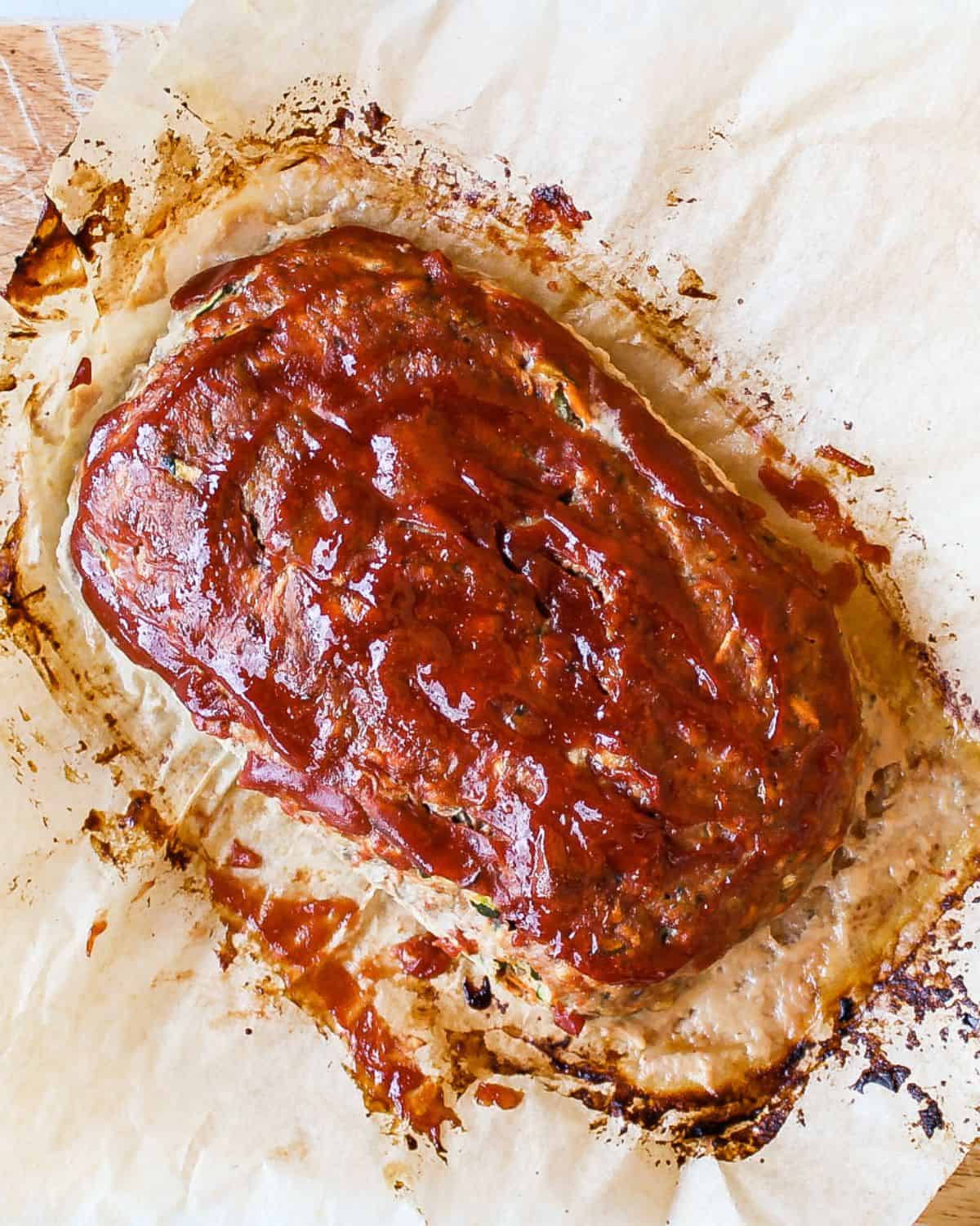 A meatloaf glazed with ketchup on top on a sheet of parchment paper.
