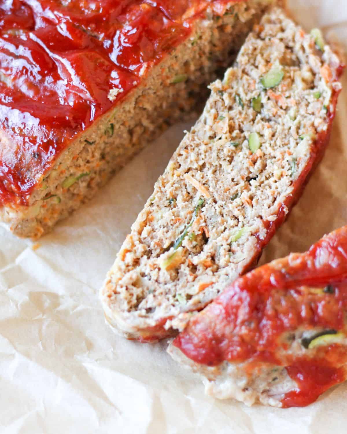 A slice of meatloaf with tomato glaze laying flat on parchment paper.