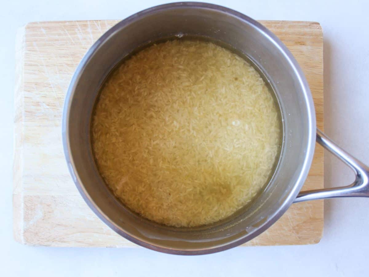 A stainless steel pot with uncooked rice and water that has yellow color due to added spices.
