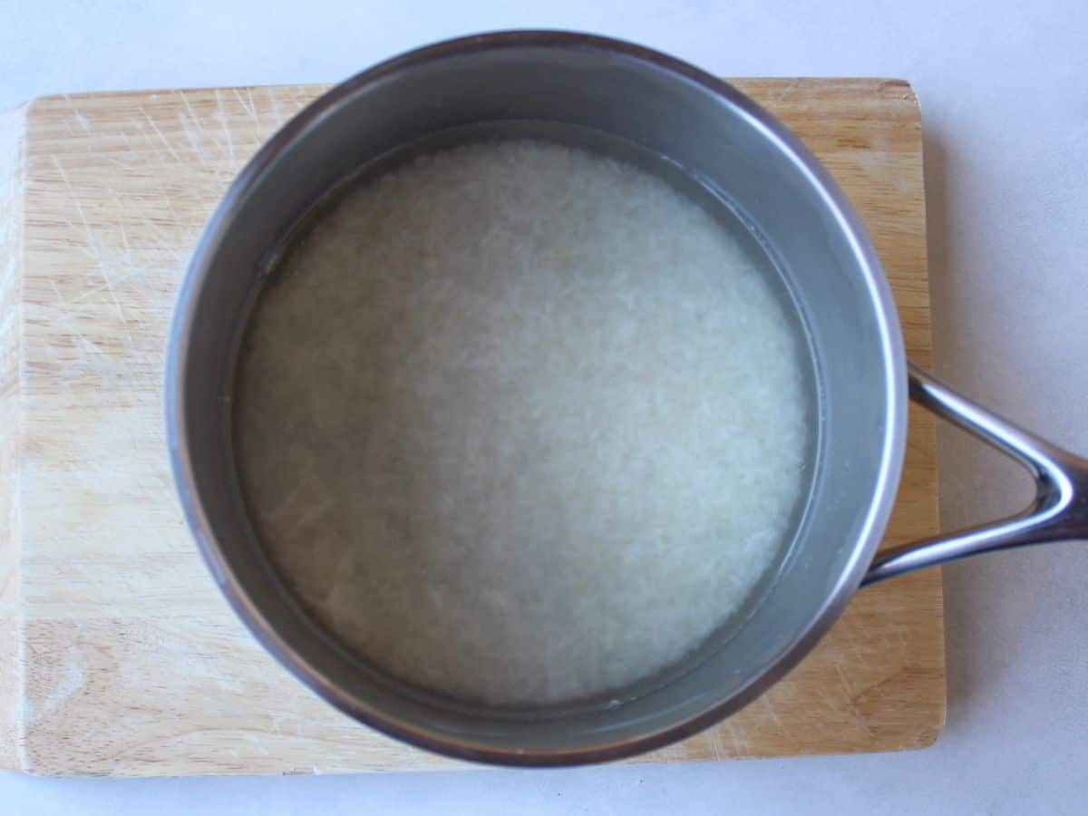 A stainless steel pot with uncooked rice and water.