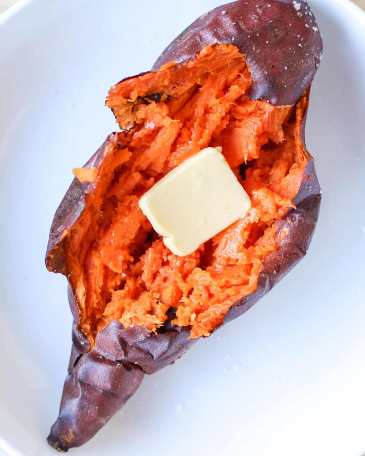 A whole baked sweet potato with bright orange flesh and a piece of butter on top.