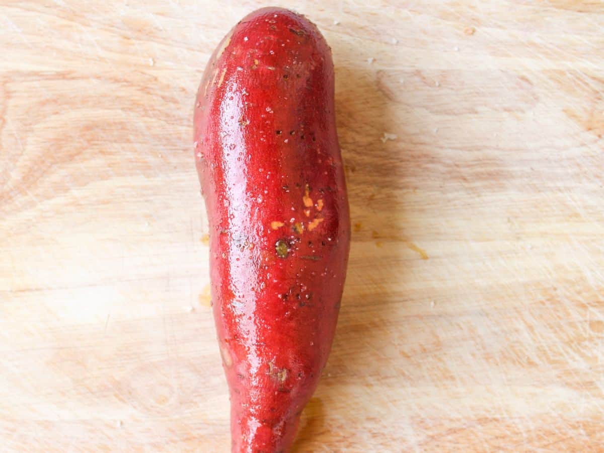 Shiny whole red sweet potato on a cutting board.