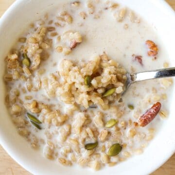 Barley grain porridge in a white bowl with added milk, pecans and pumpkin seeds.