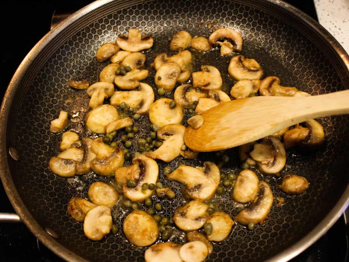 A frying pan with sliced mushrooms and capers.