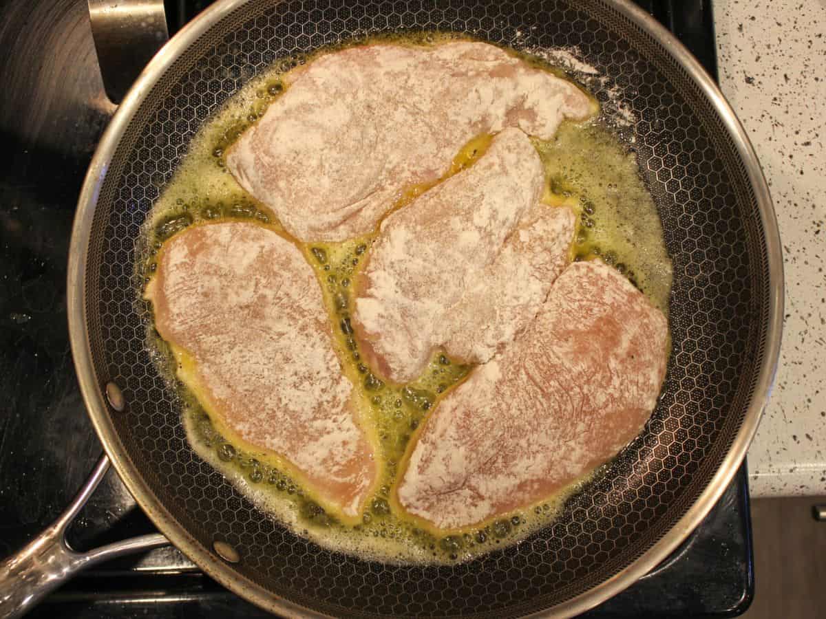 4 floured chicken breasts are searing on a frying pan.