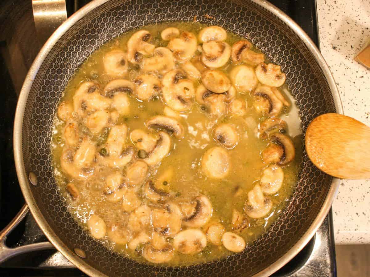 A large skillet with mushrooms capers sauce.