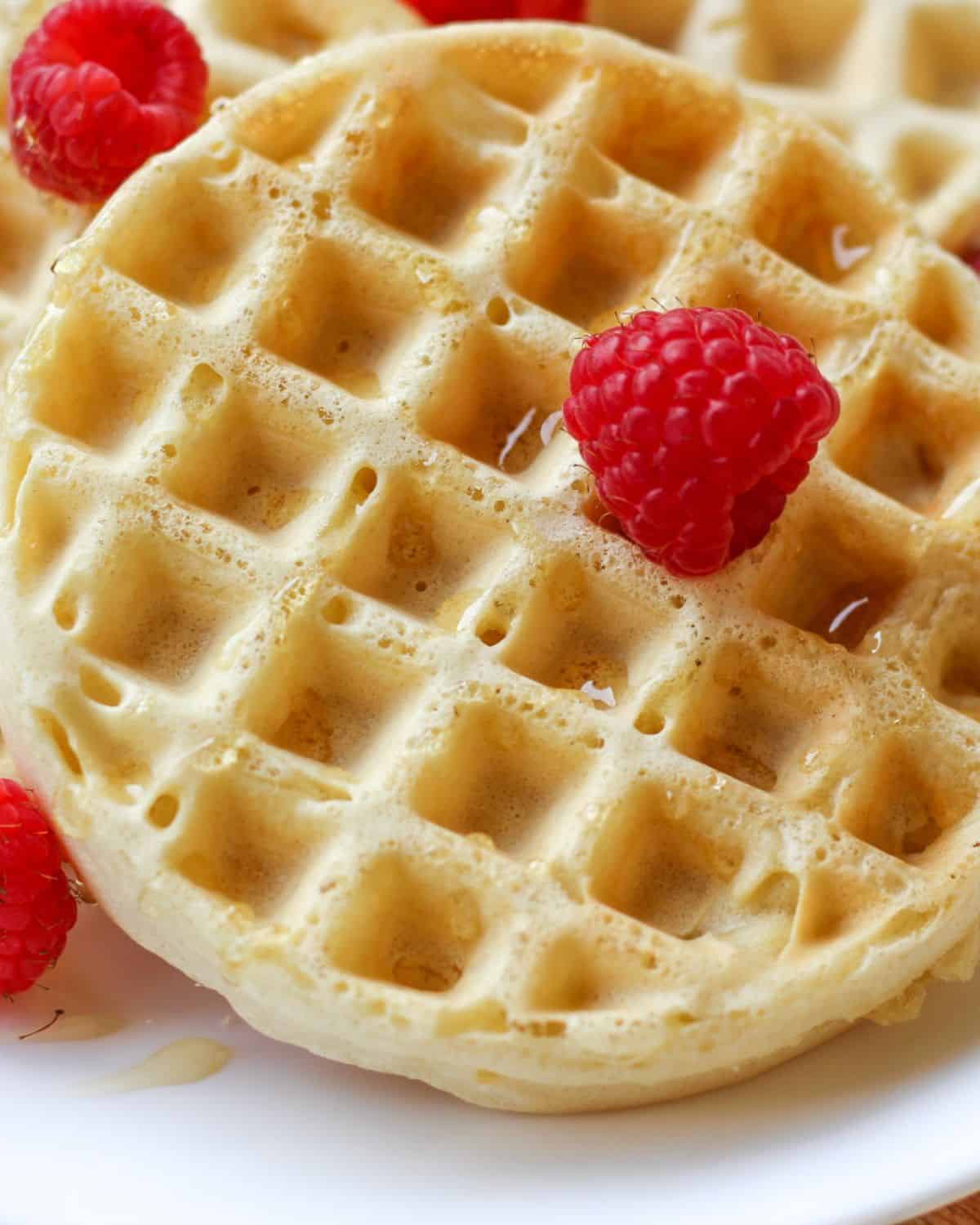 A round waffle drizzled with some syrup  and topped with a few fresh raspberries. 
