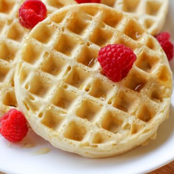 A round waffle drizzled with some syrup and topped with a few fresh raspberries.