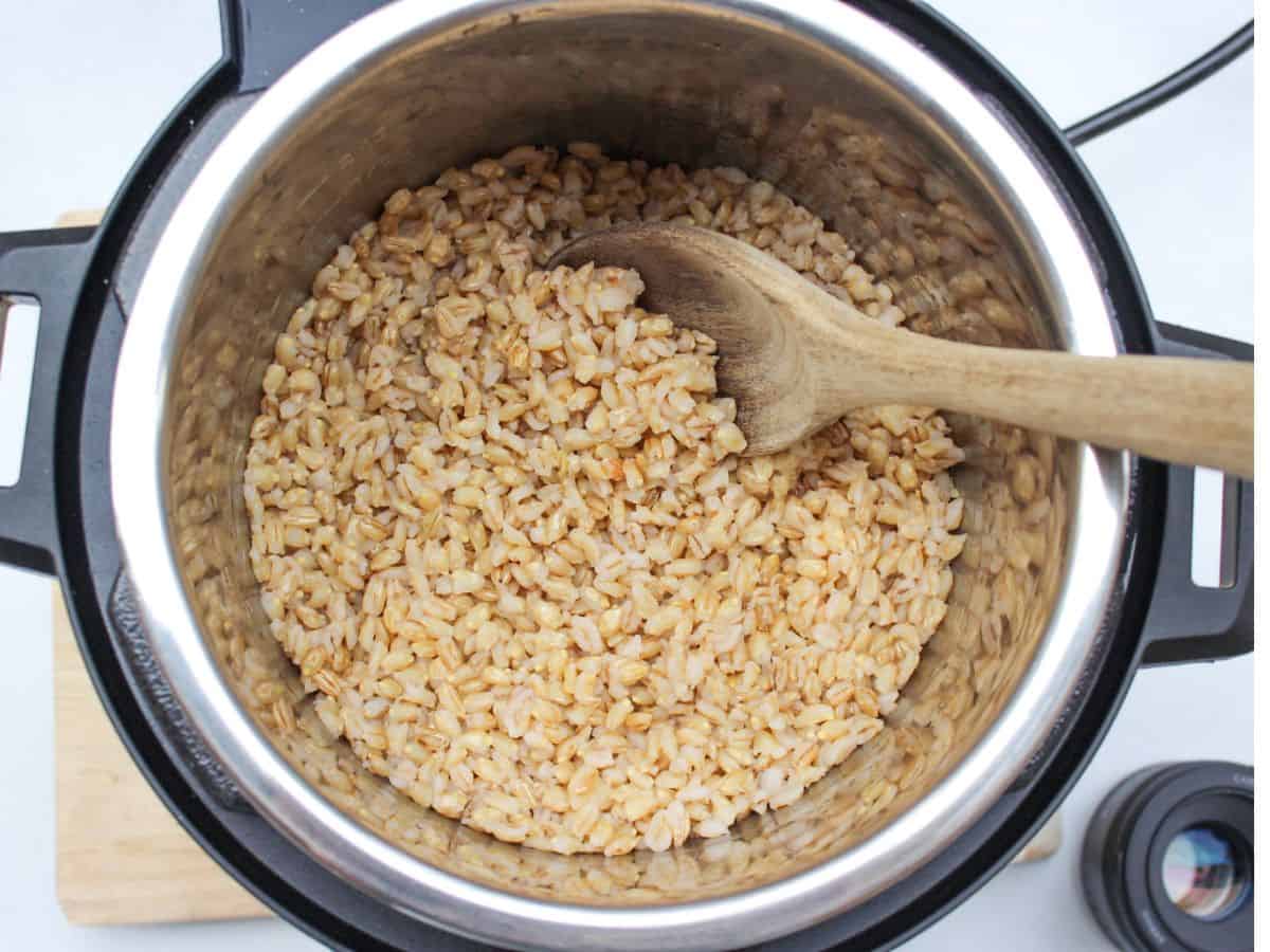 Instant pot with cooked barley grains and a wooden spoon.