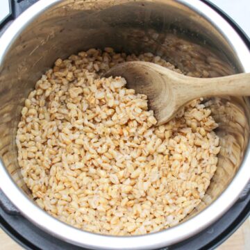 Instant pot with cooked barley grains and a wooden spoon.