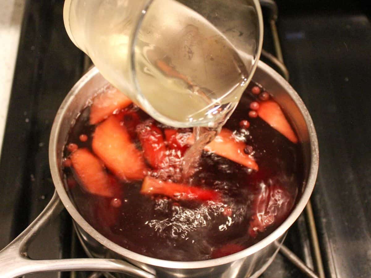 Sugar syrup is poured to the pot with simmering fruits.