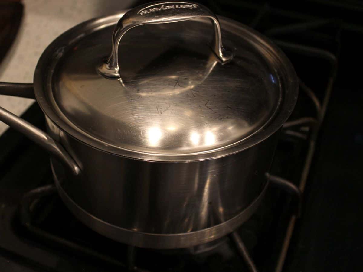 A stainless  steel pot covered with a lid on the stove.