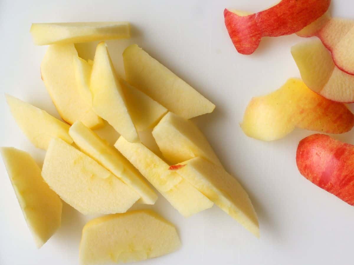 Peeled, cored and sliced apple on a white cutting board.