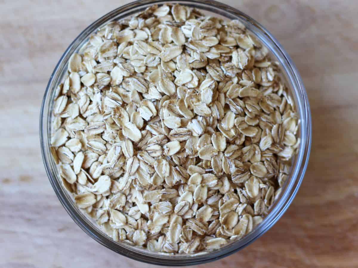 Dry oats in a glass bowl placed on a wooden surface.