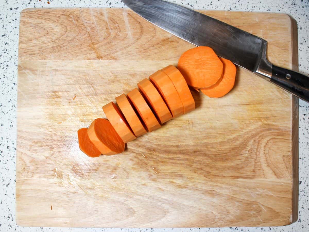 Peeled sweet potato sliced into thick rounds on a cutting board.