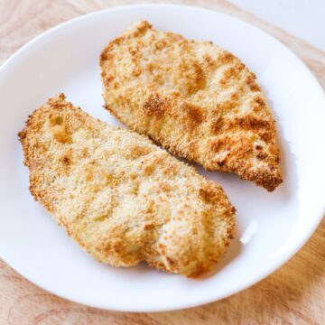 Two cooked breaded chicken cutlets on a white plate.