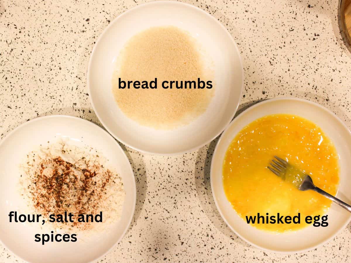 Three white shallow dishes with flour and seasoning, bread crumbs, whisked eggs.