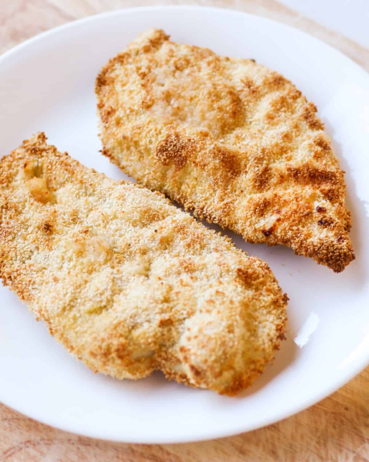 Two cooked breaded chicken cutlets on a white plate.