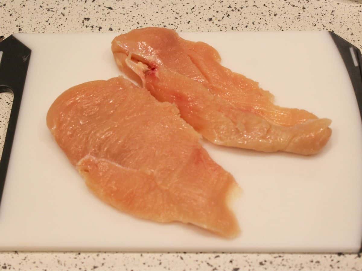 Two uncooked chicken cutlets on a white cutting board.