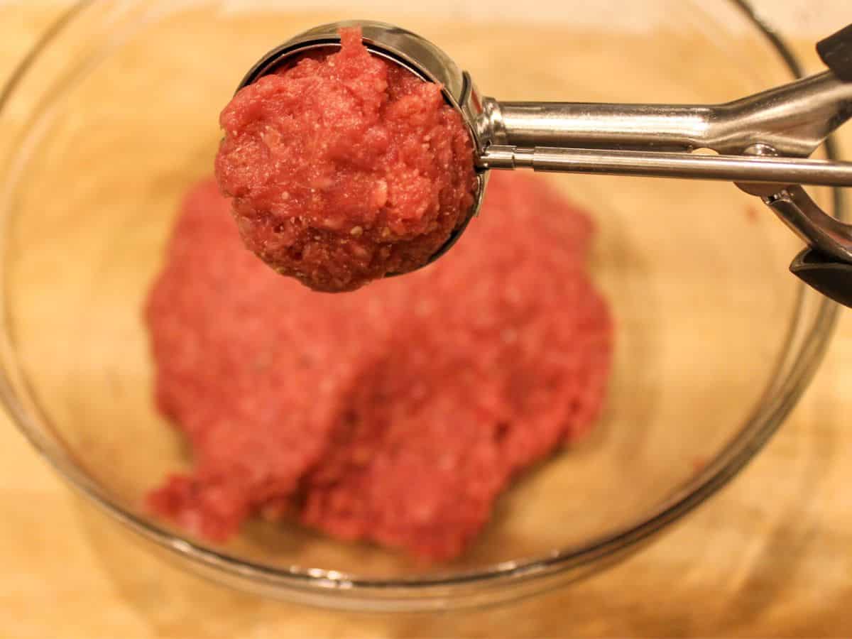 A cookie scoop filled with a meatball meat mix.
