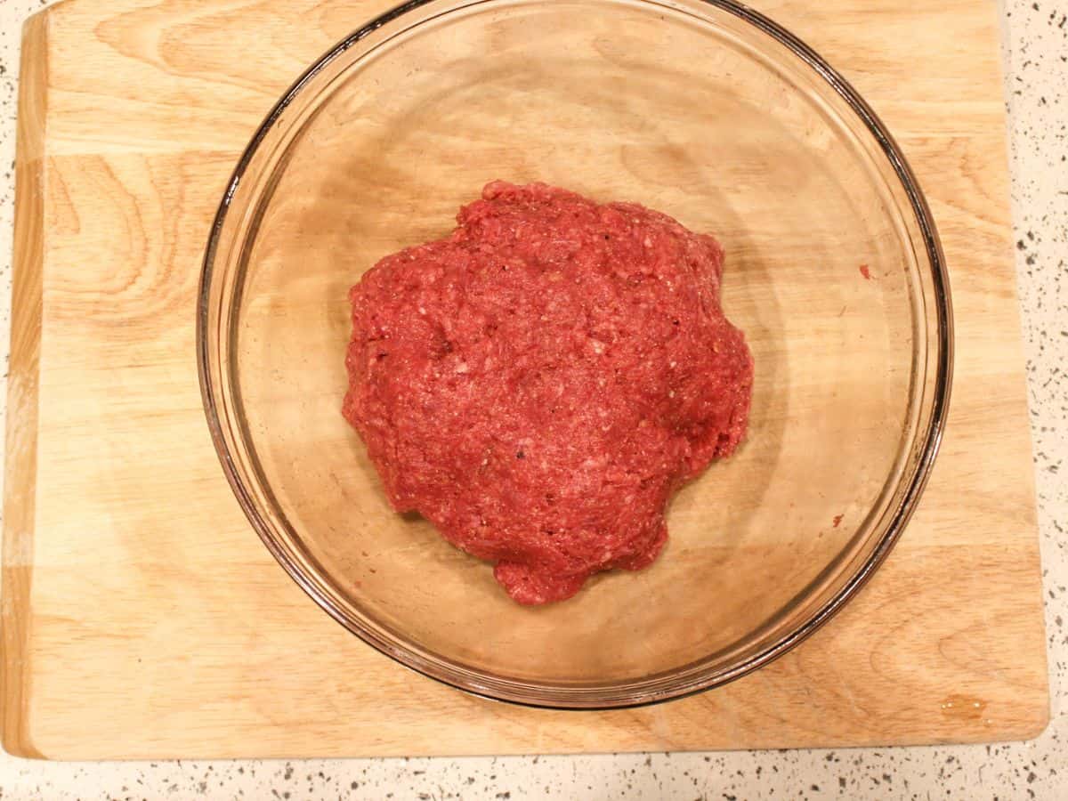 A glass bowl with raw red meat mixture.
