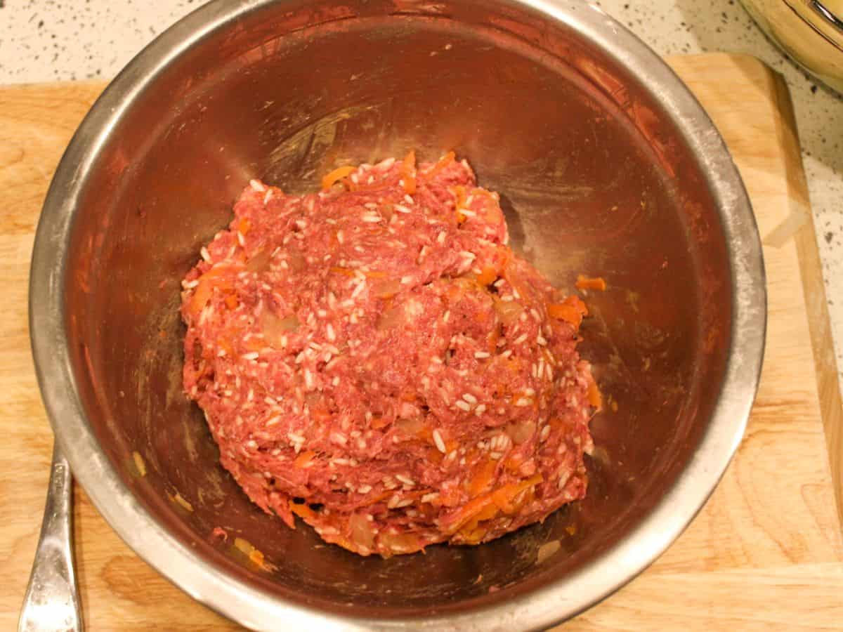 Red raw meat mixed with uncooked white rice in a large mixing bowl.