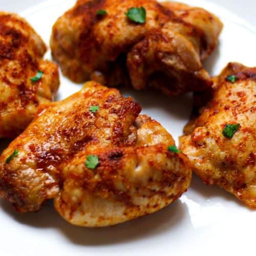 Cooked boneless skinless chicken thighs with crispy edges served on a while plate.