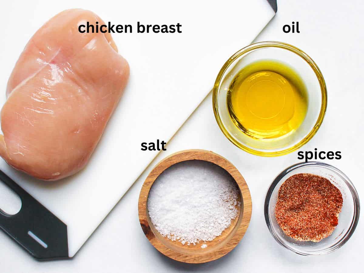 Recipe ingredients on a white surface: raw chicken breast, salt, oil, and spices.