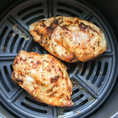 Two cooked chicken breast in a black air fryer basket.