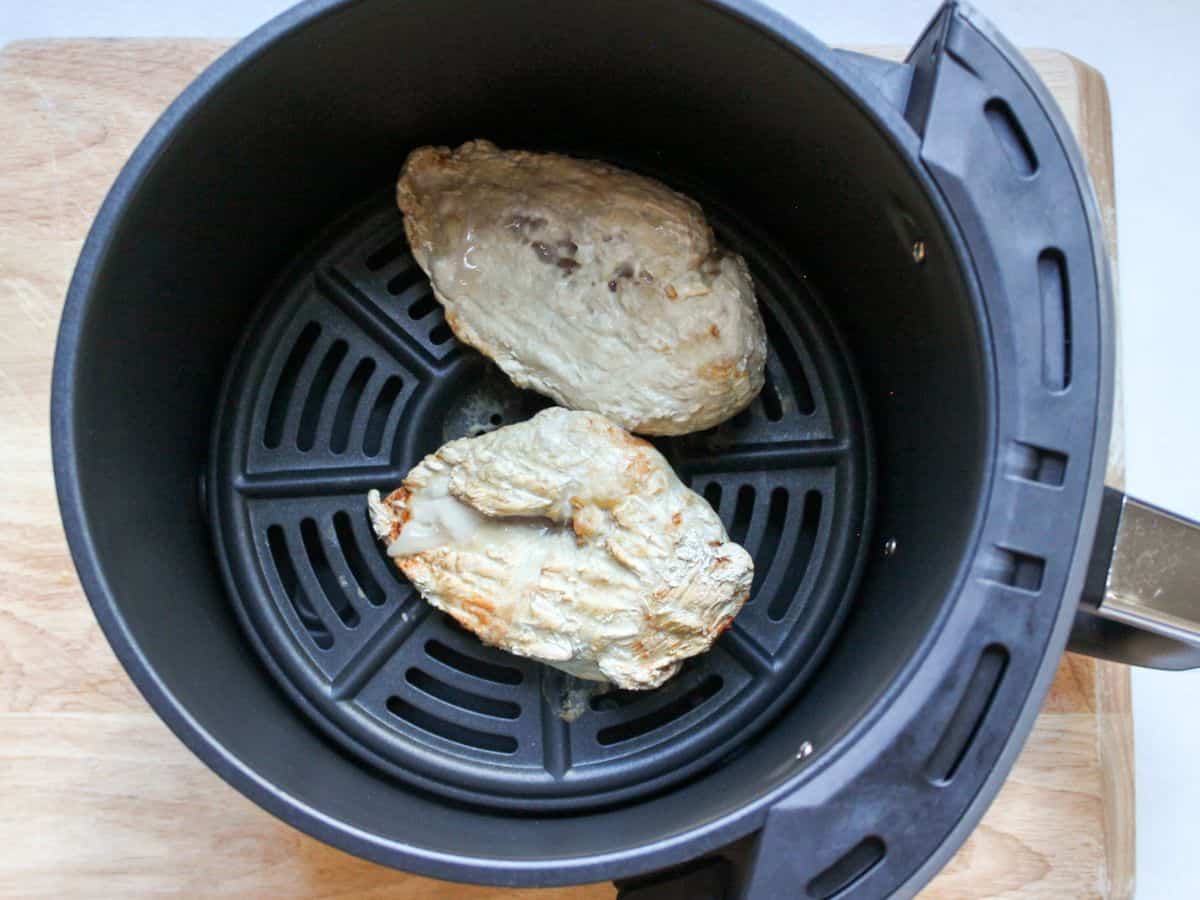 Two half cooked chicken pieces in the round air fryer basket.