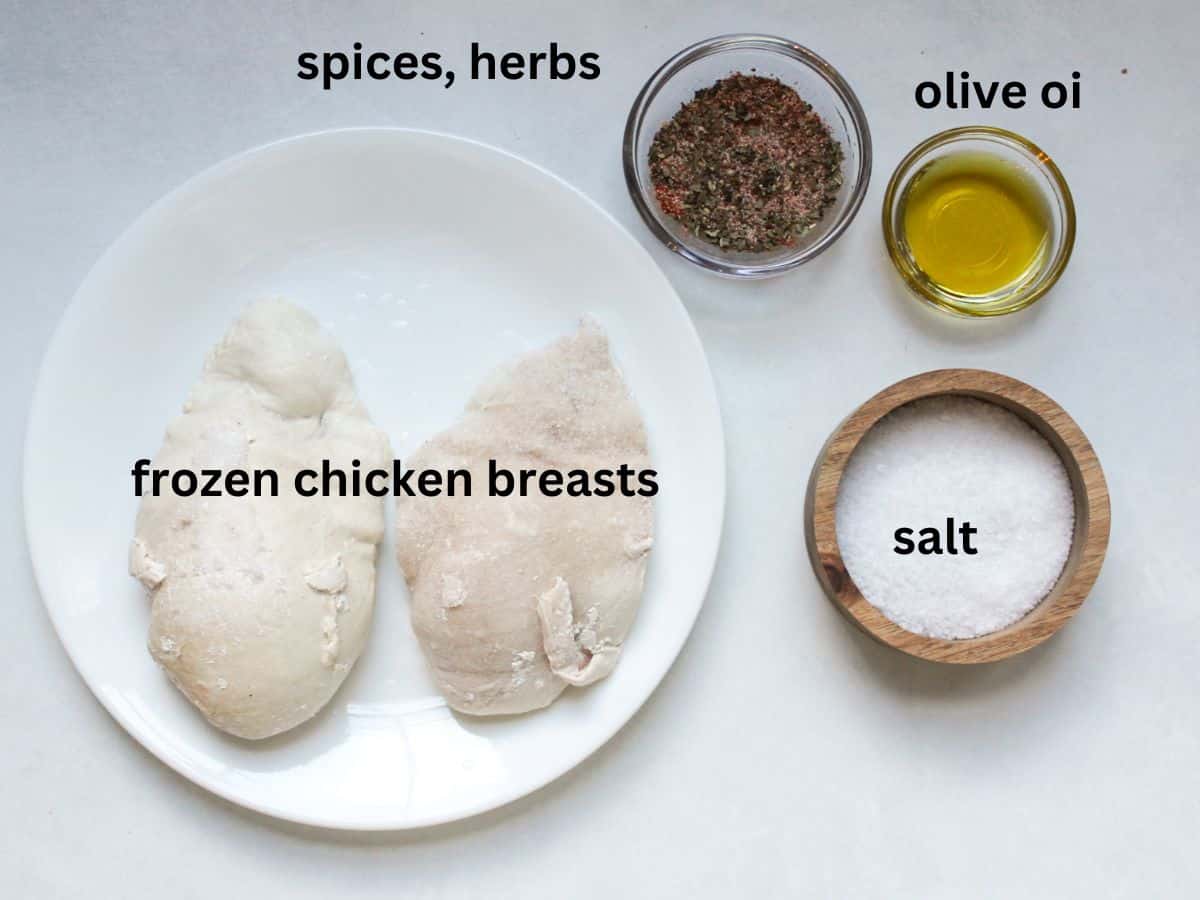 Labeled recipe ingredients on a white background. From left to right: two frozen chicken breasts, bowl with herbs and spices, olive oil, salt.