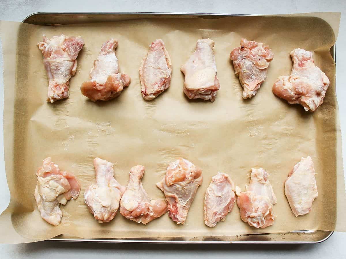 Raw chicken drumettes and wingettes arranged on a baking pan covered with parchment paper.