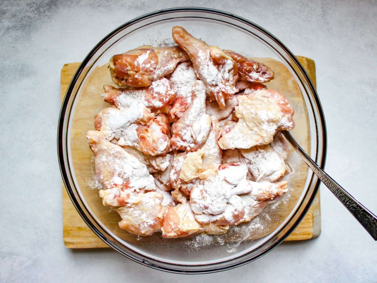 Raw chicken wings pieces covered with baking powder in a large glass bowl with a spoon in it.