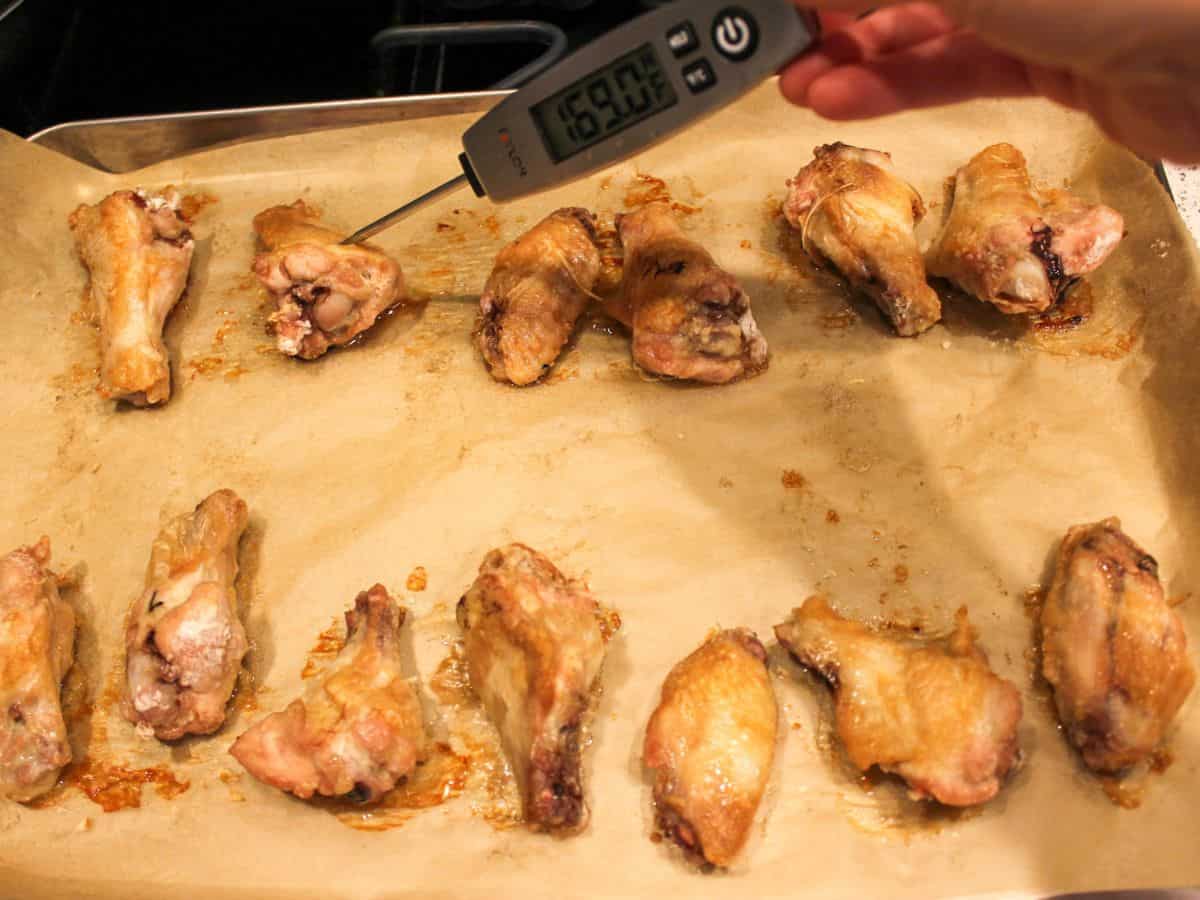 Baked chicken wings on a parchment paper with the thermometer inserted in one of the wings.