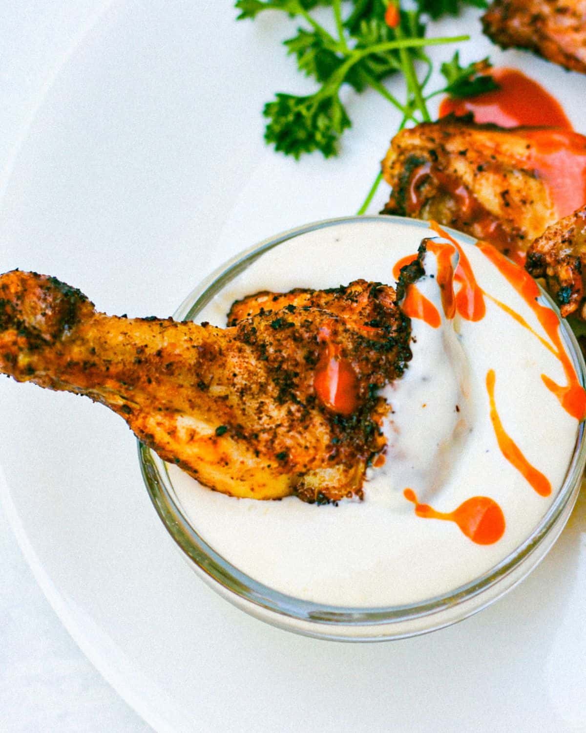 Cooked chicken drumette drizzled with red sauce and being dipped in a white creamy dressing.