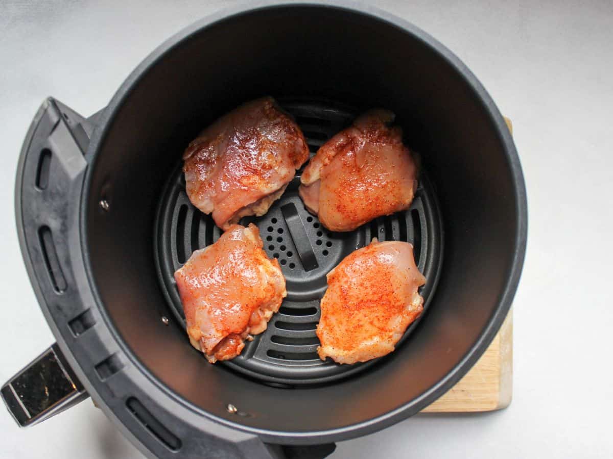 Four raw skinless thighs arranged in air fryer basket.