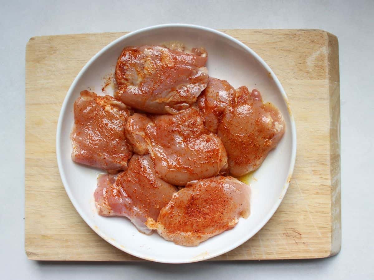 Raw seasoned skinless chicken thighs in a white shallow dish.