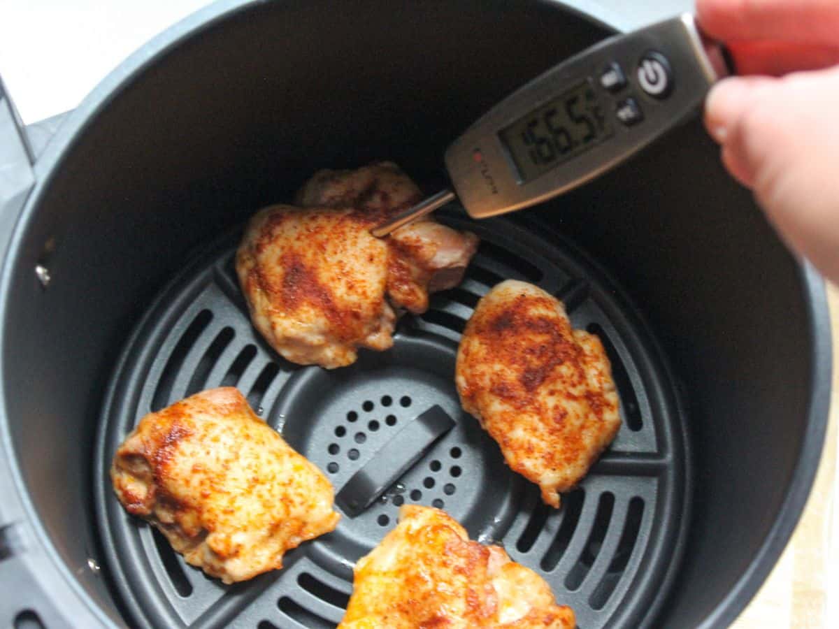 Cooked chicken thighs in air fryer basket with thermometer inserted in one of them.