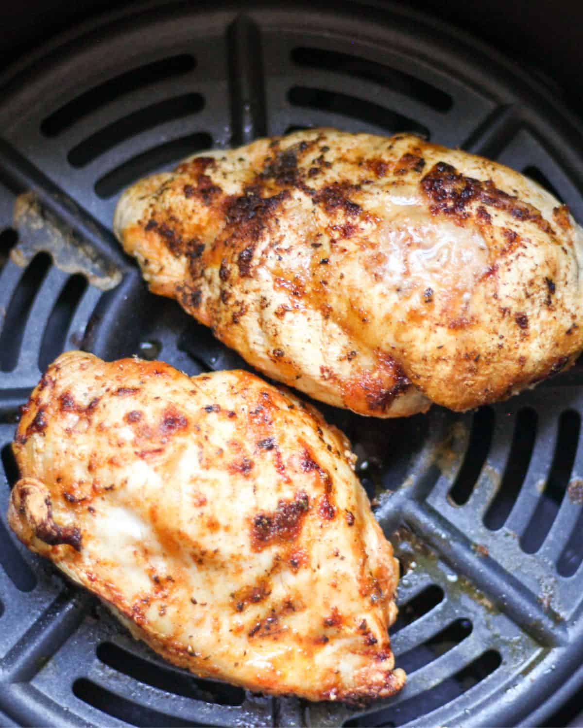 Two cooked chicken breasts on top of the round air fryer grill pan.