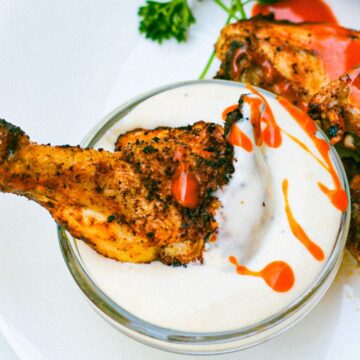 Cooked chicken drumette drizzled with red sauce and being dipped in a white creamy dressing.