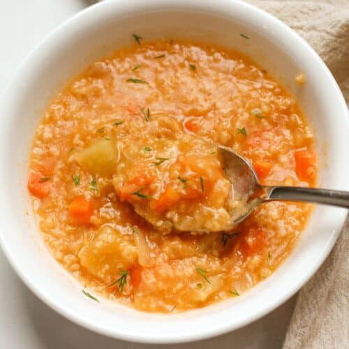 Orange cabbage soup in a white bowl with a spoon in it.
