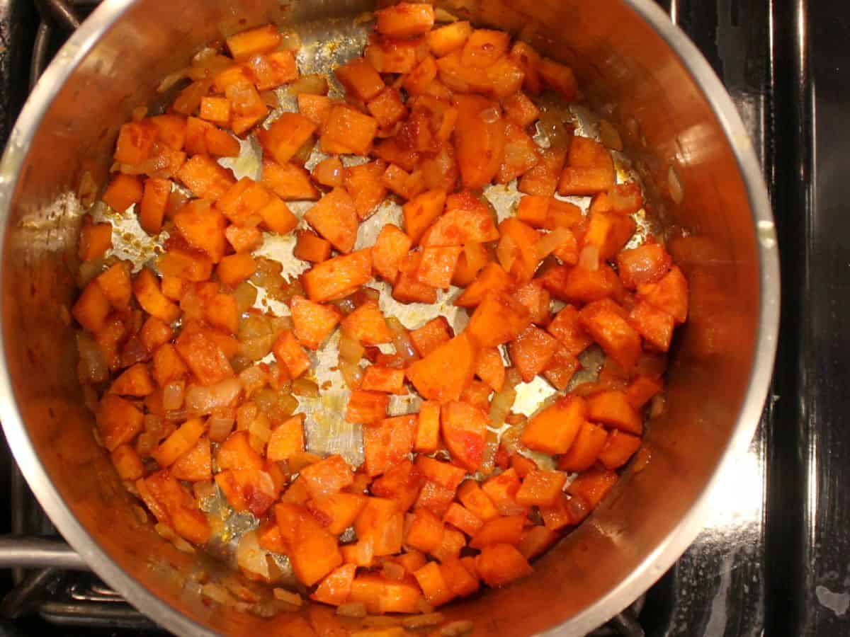 Sautéed diced onions and carrots with some tomato paste in a stainless steel pot.
