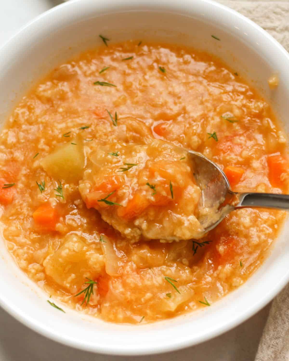 Orange cabbage soup in a white bowl with a spoon in it.