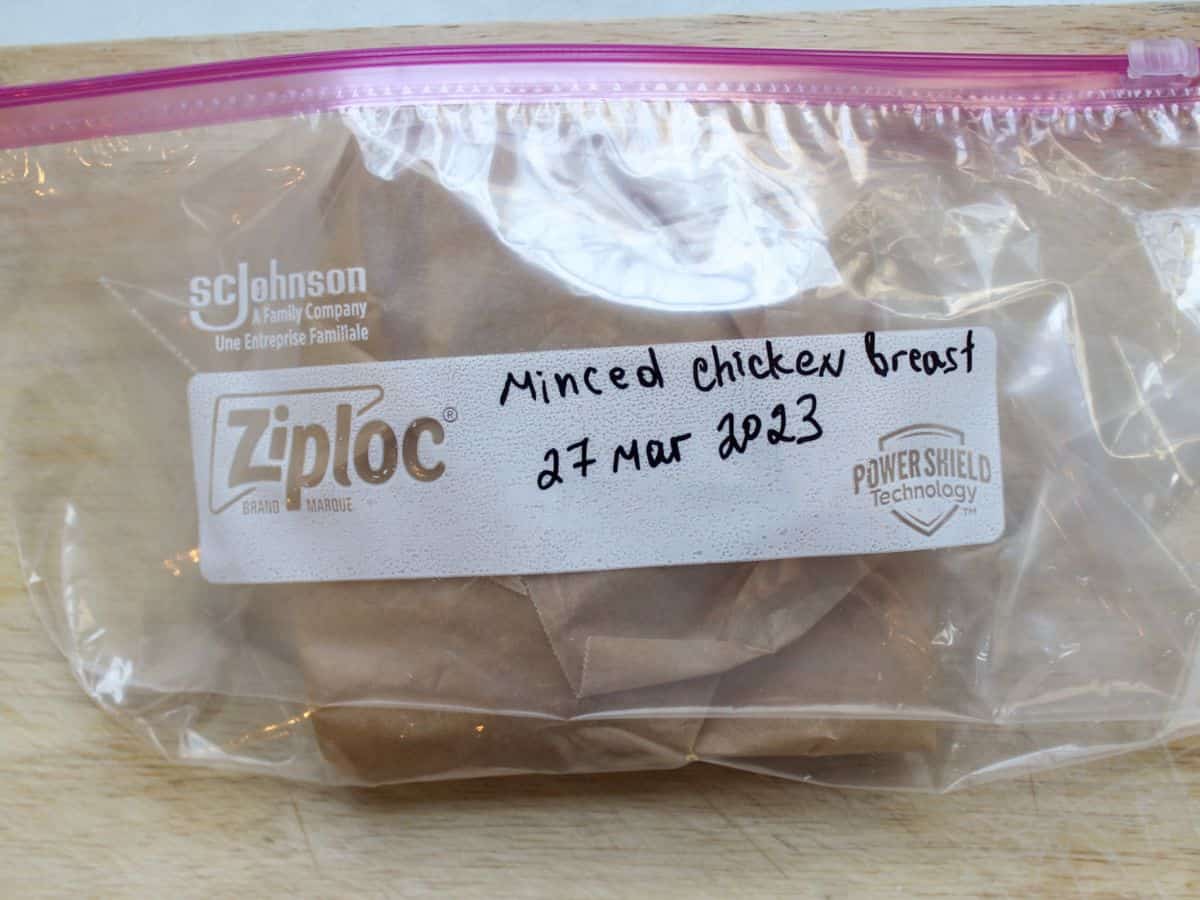 A Ziploc bag with content wrapped in parchment paper inside. The bag labeled as "minced chicken breast 27 Mar 2023" with a black marker.