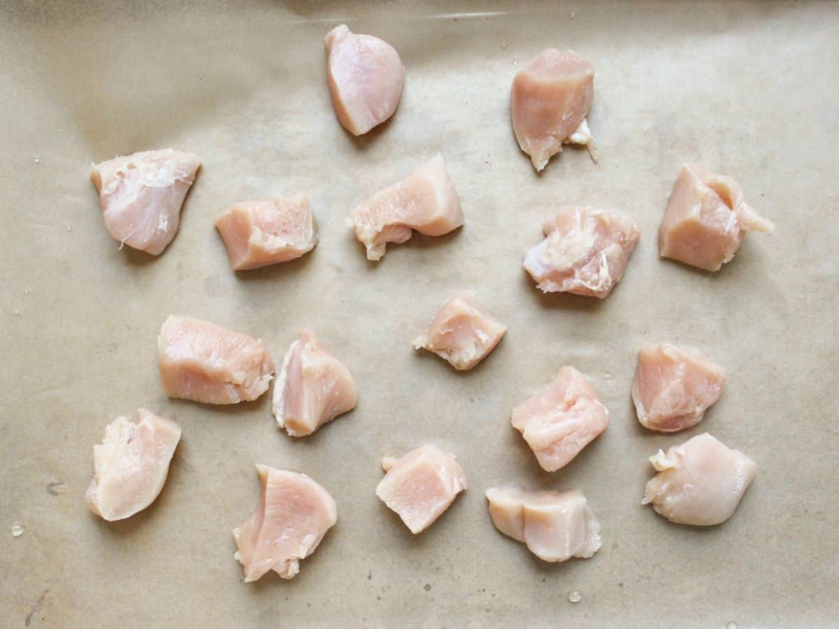 Chunks of raw chicken meat arranged on a parchment paper.