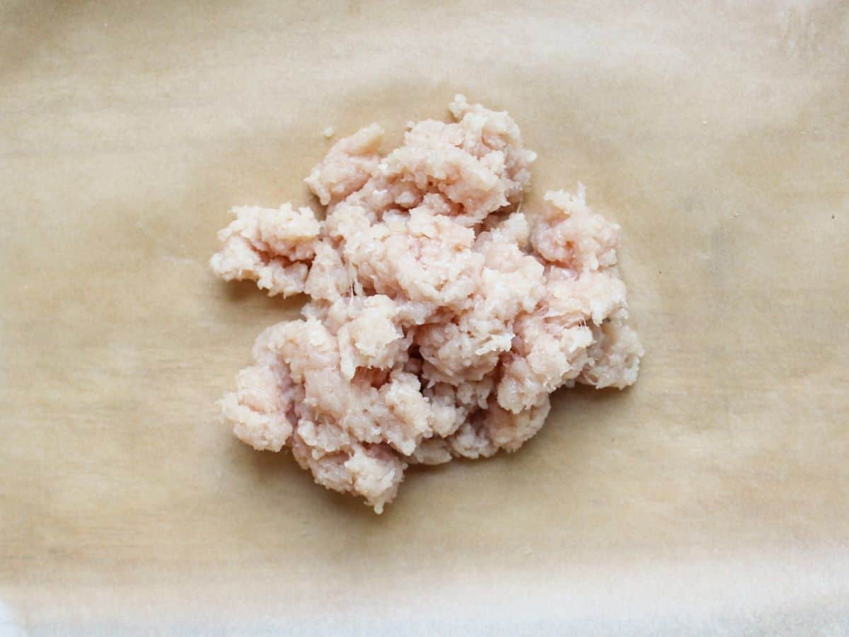 Piled raw ground chicken on a parchment paper.