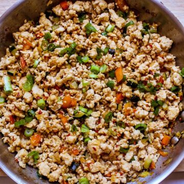 Chicken mince stir fry garnished with green onions in a stainless steel frying pan.